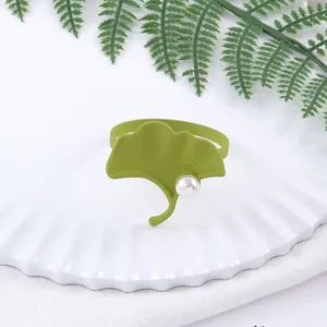 Detalle de servilletero con hoja de ginkgo verde mate y perla sobre un plato blanco puro