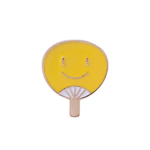 Détail macro d'un pin's éventail émaillé jaune avec un motif de visage souriant