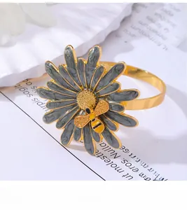 Close-up of golden daisy flower napkin ring with grey enamel petals and bee detail