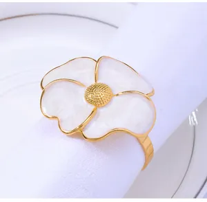 Detailed view of white enamel flower napkin ring with gold center on a white cloth