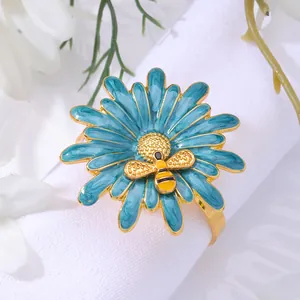 Daisy and bee napkin ring with blue enamel petals and gold plating on a white linen napkin
