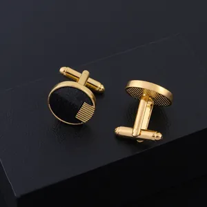 Boutons de manchette ronds dorés et noirs avec motif rayé sur une boîte texturée