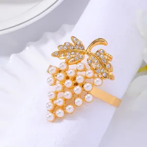 Servilletero de uva dorada con perlas blancas y diamantes sobre servilleta blanca