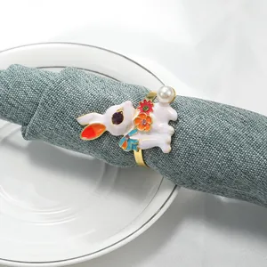 Servilletero de conejo dorado con flores esmaltadas y perla sobre servilleta verde