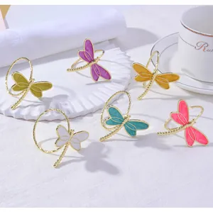 Set of six colorful enamel dragonfly napkin rings on a white plate with elegant gold trim