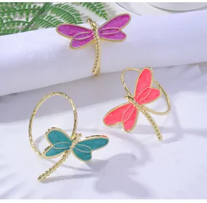 Detailed macro of gold dragonfly napkin rings with colorful enamel wings on white fabric
