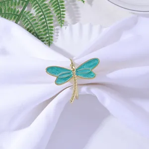 Detailed view of a golden dragonfly napkin ring with teal enamel wings on white fabric