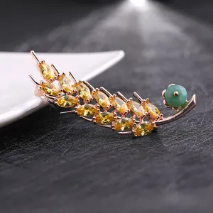 Vue macro d'une broche épi or rose avec pierres jaunes et perle turquoise