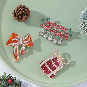 Three-piece Christmas brooch set with red bow, golden bells, and Happy Holidays lettering