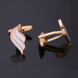 Macro detail of gold wing cufflinks with white enamel on a reflective black surface