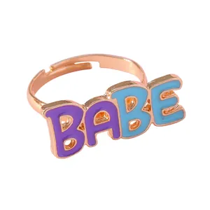 Détail d'une bague dorée réglable avec lettres en émail BABE violettes et bleues