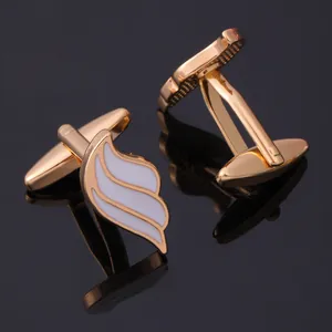 Macro view of gold winged cufflinks with white enamel inlay on a black reflective surface