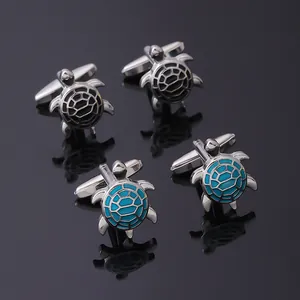 Detailed close-up of turtle-shaped cufflinks in black and turquoise enamel on a reflective surface