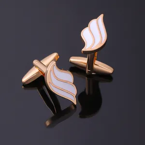 Detail of gold wing-shaped cufflinks with white enamel on a black reflective surface