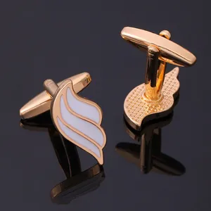 Golden wings cufflinks with white enamel inlay shown with elegant reflection on dark surface