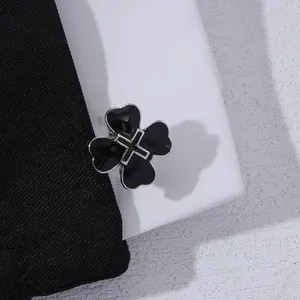 Detail of a black four-leaf clover cufflink with a silver cross on fabric texture