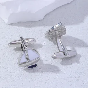 Macro shot of silver sailboat cufflinks with white enamel detail on stone texture