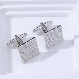 Detailed close-up of square silver cufflinks with intricate micro-grid metal texture