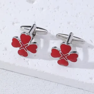 Silver cufflinks with red four-leaf clover heart design on a white textured stone base