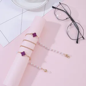 Close-up of golden clover eyeglass chain with white pearls and purple floral charms