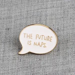Primer plano de pin de esmalte dorado con el texto The Future Is Naps sobre tela