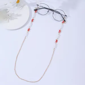 Detail of gold eyewear chain with red butterfly charms and white pearls on black glasses