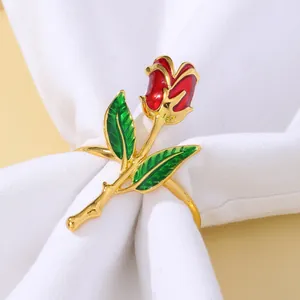 Elegante servilletero de oro con rosa de esmalte rojo y hojas verdes sobre lino blanco