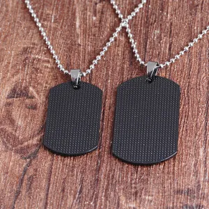 Detail of matte black dog tag necklaces with textured dots on dark wood background
