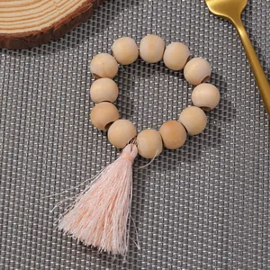Boho-Serviettenring aus Holzperlen mit rosa Quaste auf grauem Set und goldener Gabel