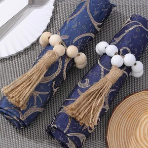 Close-up of wooden bead napkin ring with jute tassel on a navy blue textured fabric napkin