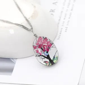 Vue rapprochée d'un collier pendentif ovale avec fleurs séchées roses et arbre de vie