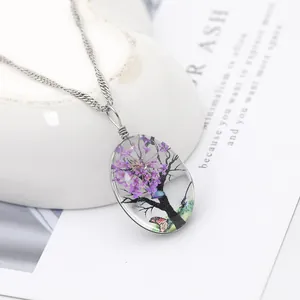 Vue macro détaillée d'un pendentif ovale en verre avec fleurs séchées mauves et arbre de vie