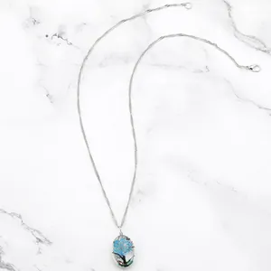 Vue macro d'un pendentif ovale en verre avec fleur séchée bleue sur marbre blanc