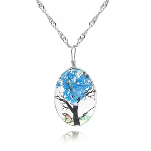 Macro de la chaîne argentée et du pendentif ovale avec fleurs séchées bleues et motif d'arbre