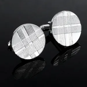 Macro detail of silver round cufflinks with cross-line texture on black reflective surface