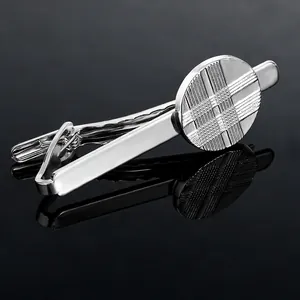 Close-up of silver tie clip with engraved circular grid pattern on black background