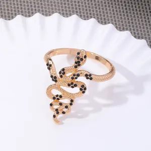 Golden snake napkin ring with black rhinestones on a white plate and grey background
