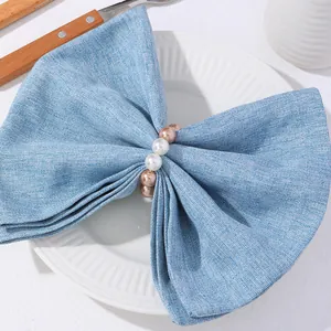 Primer plano de servilletero con perlas champán sobre servilleta de lino azul y mesa decorada