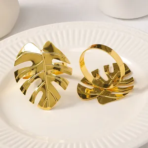 Servilletero metálico dorado con forma de hoja de monstera sobre plato de cerámica