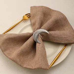 Close-up of silver crescent moon napkin ring with ribbed texture on a brown linen napkin