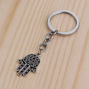 Vintage silver Hamsa Hand keychain with intricate floral engravings on a rustic wood backdrop