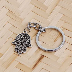 Vintage silver Hamsa hand keychain with hollow floral pattern on woven background