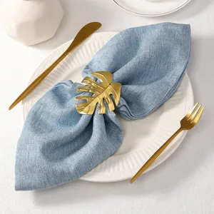 Primer plano del servilletero dorado de hoja de monstera sobre tela azul elegante