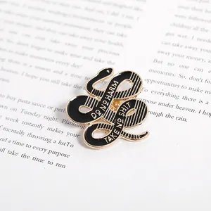 Detailaufnahme der Schlangen-Emaille-Anstecknadel mit Spruch auf einer Buchseite