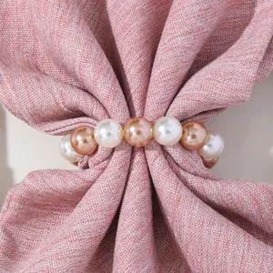 Detalle de servilletero con perlas blancas y champán sobre tela con textura rosa