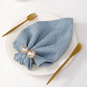 Dettaglio portatovagliolo con perle color champagne su un tovagliolo in lino azzurro