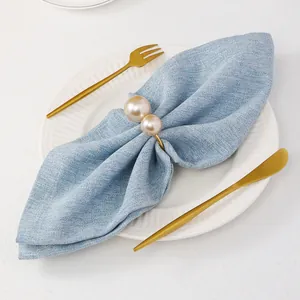 Dettaglio macro del portatovagliolo a U dorato con perle champagne su lino blu