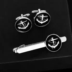 Men's silver anchor cufflinks and tie clip set with black enamel on a textured background