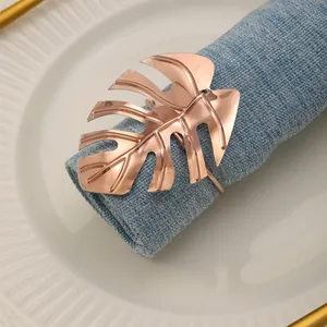 Primer plano del servilletero hoja monstera oro rosa sobre servilleta de lino azul