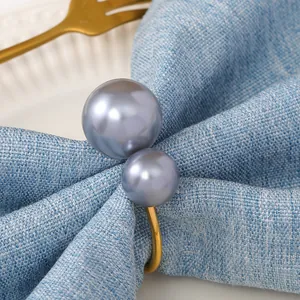 Portatovagliolo a U color oro champagne con perle grigie su tovagliolo di lino blu